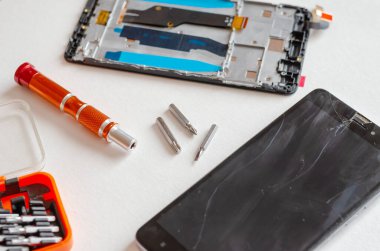Açık bir yüzeyde kırık ekranı ve el aleti olan akıllı bir telefon. Bozuk ekranlı siyah telefon. Servis Tamiri. Seçici odak.