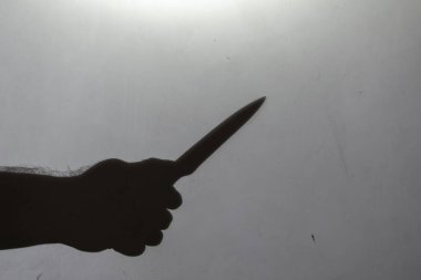 Görüntü, bulanıklık, gürültü, tahıl etkisi. Açık gri bir duvarda elinde bıçak olan bir adamın koyu renk silüeti. Kapalı alanda. Seçici odak.