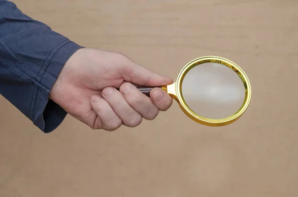 Vuxen Man Håller Ett Förstoringsglas Handen Mot Brun Bakgrund Ett — Stockfoto