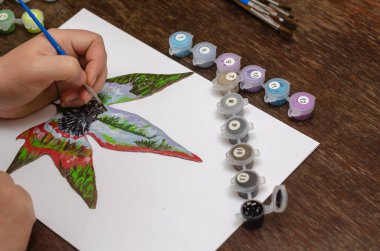 Bir kadının eli kuru bir akçaağaç yaprağını boyar. Akrilik ve guaj boyalı küçük bir kirpi çiziyorum. İçeride. Seçici odak.