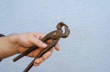 Bir adam elinde eski maşaları tutuyor. Paslı metal bir el aleti. Yakın plan. Seçici odak.