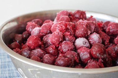 Metal bir kasede taze donmuş kırmızı kiraz meyveleri. Buz ve buzla kaplı dutlara yakın çekim. Seçici odak.