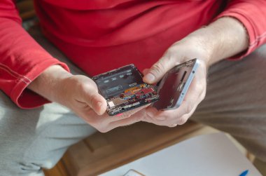 Yetişkin bir erkek akıllı telefonu söküyor. Eller arka koruyucu kapağı ekrandan ayırıyor. Telefon tamiratı ve bakımı. Elektronik atıkları ayıklıyorum. Yakın plan. Seçici odak.