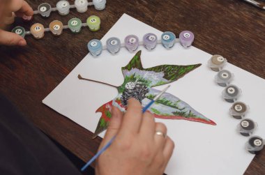 Kuru odun yaprakları üzerinde çizim yapmak. Yaratıcılık, resim. Yetişkin bir kadın ormanda yürürken tatlı bir kirpi çizmek için akrilik kullanıyor. İçeride. Seçici odak.