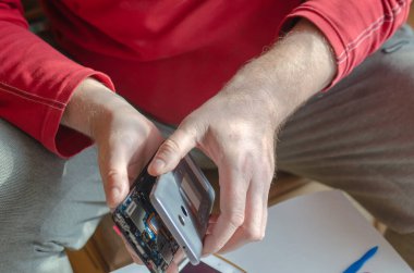 Yetişkin bir erkek akıllı telefonu söküyor. Eller arka koruyucu kapağı ekrandan ayırıyor. Telefon tamiratı ve bakımı. Elektronik atıkları ayıklıyorum. Yakın plan. Seçici odak.