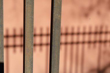 Bir çitin gölgeleri düzensiz bir mercan arka duvarı. Metal parmaklıkların koyu gölgeleri. Binanın dış kısmının dekoratif sıvası. Seçici odaklanma. Kimse yok..