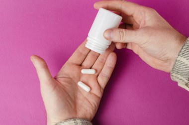 Bir adam avucunun içine açık beyaz plastik bir şişeden ilaç döküyor. İlaç ve sağlık hizmetleri. Yukarıdan bir açıdan bak. Seçici odak.