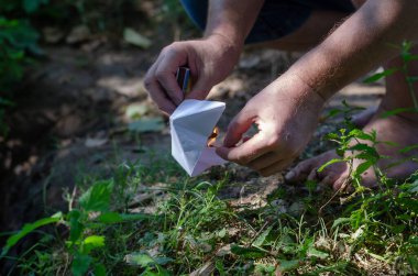 Çıplak ayaklı yetişkin bir adam kağıttan bir tekne yakıyor. Beyaz bir çocuk origami teknesi ve yanan bir kibrit tutan eller. Yaz zamanı. Seçici Numara. Odanın dışında..
