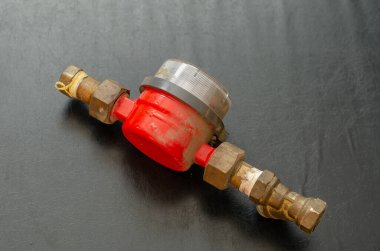 An old dusty water meter on a black background. Red device for counting the volume of water passing through the water supply. Selective focus. No people.