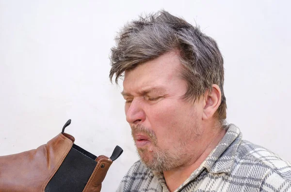 The man smelled an unpleasant odor from his brown boot. A male with disheveled hair against the light gray wall. Indoors. Selective focus.