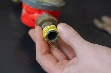 Adamın eli pirinç musluğun yanındaki su göstergesini sarı bir ambalajla tutuyor. Siyah zemin üzerinde parçalanmış kırmızı cihaz. Tesisatçı servisi. Yakın plan. Seçici odaklanma. Kimse yok..