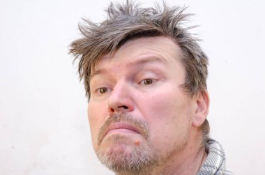 Dağınık saçlı, şaşkın bir kocanın portresi. Yüzünde somurtkan bir suratla parlak bir duvara yaslanmış yetişkin bir adam. Odanın içinde. Seçici odak.