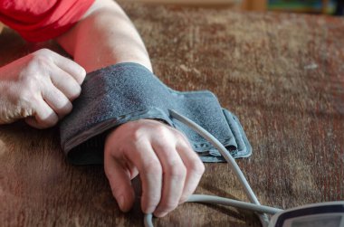 Evde tansiyonunu ölçüyorum. Yetişkin bir erkek kolunun ön kısmına dijital tansiyon monitörü takar. Odanın içinde. Seçici odak.