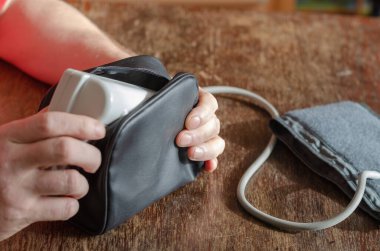 Adamın elleri siyah bir kesekağıdına yerleştirilmiş dijital kan basıncı monitörüne. Kahverengi ahşap bir masada tıbbi bir cihaz. Evde kan basıncını ölçüyorum. Odanın içinde. Seçici odak.