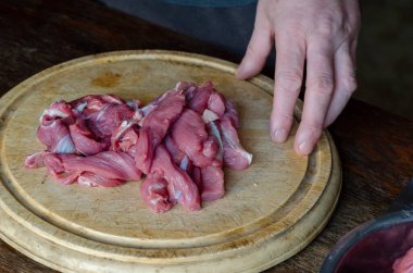 Tahta kesme tahtasındaki çiğ sığır eti şeritleri. Bir adamın eli çiğ etle birlikte kesme tahtasından tutar. Seçici Odaklanma.