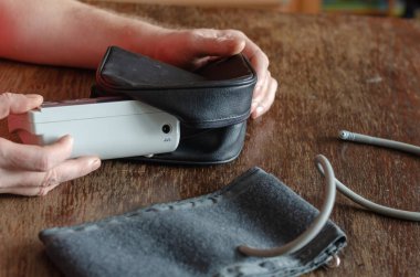 Adamın elleri siyah bir kesekağıdına yerleştirilmiş dijital kan basıncı monitörüne. Kahverengi ahşap bir masada tıbbi bir cihaz. Evde kan basıncını ölçüyorum. Odanın içinde. Seçici odak.