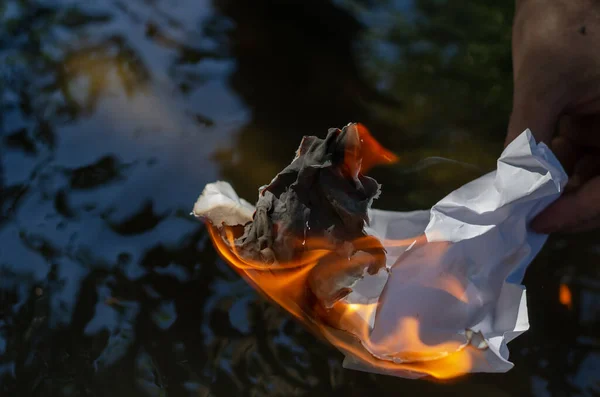 男の手の中で燃える紙のしわの部分 川や川の表面に手で燃える白い紙を砕いた 選択的焦点 — ストック写真