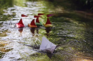 Mutfak süngerlerinden yapılmış gemiler beyaz kağıt bir geminin peşindeler. Çocuk yelkenli yarışı. Küçük bir nehirde ya da derede seyreden çocukların ev yapımı tekneleri. Oyuncak. Yaz zamanı. Seçici odak.