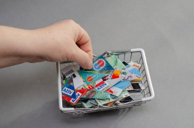 Bir kadının eli, alışveriş arabasından banka kartının bir parçasını çıkarır. Çeşitli bankalardan kesilmiş kredi kartlarıyla dolu metal alışveriş arabası gri bir arka planda. Kiev, Ukrayna - 01 05 2022.