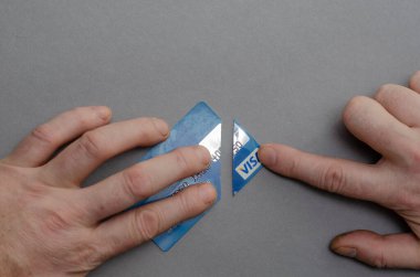 İki adamın eli kesilmiş bir Visa banka kartını ayırıyor. Gri bir arka plana karşı mavi bir kredi kartı. Seçici odaklanma. Kiev, Ukrayna - 01 05 2022.