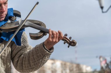 Konser sırasında bir sokak müzisyeninin portresi. Elektronik bir kemanla klasik müzik çalan olgun bir adam. Kafasında Audi logosu olan siyah bir beyzbol şapkası. Ukrayna, Nikolaev - 02 19 2022