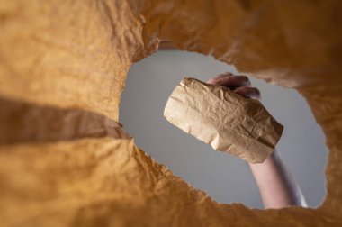 Bir el, kağıttan bir öğle yemeğini kese kağıdına koyar. Olgun bir adamın eli açık kahverengi torbanın üzerinde yiyeceği tutuyor. Tepeden tırnağa vurulmuş. Kapatın. Seçici odak.