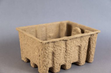 Bastırılmış kartondan yapılmış boş kahverengi bir kap. Gri arkaplana karşı mühür veya geri dönüşüm tepsisi.