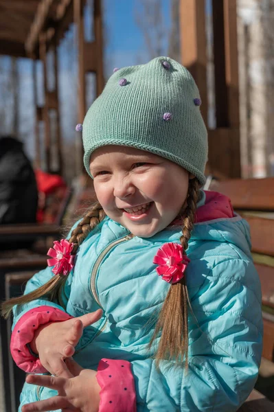 Parktaki bankta oturan pozitif bir çocuğun portresi. Uzun örgülü ve çiçek şekilli fiyonklu gülen kız. Beş yaşında halinden memnun bir çocuk. İlkbahar.