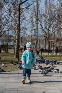 Mavi ceketli anaokulu çağında bir kız şehrin güvercin sürüsünün önünde kendi etrafında dönüyor. Ellerini cebinde tutan uzun at kuyruklu beş yaşındaki bir çocuğun portresi. Güneşli bahar günü.