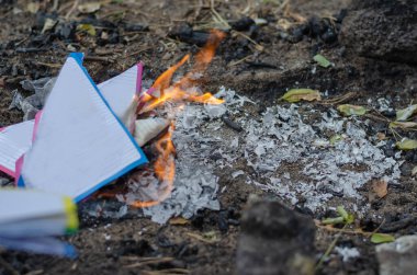 Yırtık defter kağıtlarını yakıyor. Çok renkli çarşaflar gri küle dönüşür. Odanın dışında. Seçici Odaklanma.