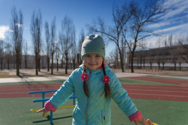 Spor sahasında eğlenen bir çocuğun portresi. Uzun at kuyruklu beş yaşında bir kız. Çocukluk. Dışarı çıkın. Güneşli bir bahar günü.