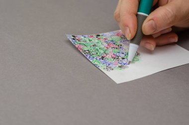 Bir kadının manikürsüz eli kalemle soyut bir resim çizer. Farklı geometrik şekillerde çok renkli bir desen. Yakın plan. Seçici odak.