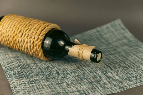 A bottle of red wine wrapped in yellow rope. The bottle is corked.