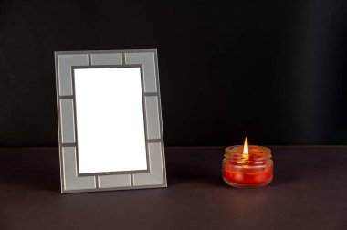 Boş bir dikey fotoğraf çerçevesi ve koyu bir arkaplanda yanan bir mum. Dikdörtgen gümüş fotoğraf çerçevesi ve yuvarlak cam şeffaf bir kavanozda kırmızı mum..