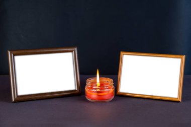 Yanan mumun yanındaki siyah hasarlı alana karşı iki boş fotoğraf çerçevesi. Cam bir kavanozda kırmızı mum yanıyor. Yatay olarak düzenlenmiş tahta dikdörtgen fotoğraf çerçeveleri.