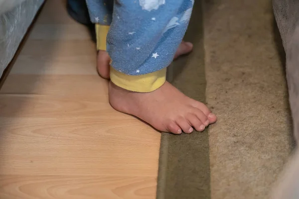 一个赤脚站在卧室地板上的孩子的下部 一个身穿蓝色睡衣的5岁男孩站在铺满地毯的地板上他的床边 — 图库照片