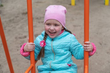 Uzun at kuyruklu mutlu bir kız salıncakta sallanıyor. Beş yaşında bir çocuk oyun parkında dünya umurunda olmadan oynuyor..