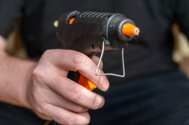 Yapıştırıcı tabancası tutan bir adamın yakın çekimi. Elinde el aleti olan yetişkin bir adam..