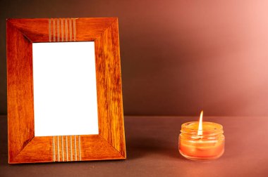 Geniş kahverengi bir fotoğraf çerçevesi yanan bir mumun yanındaki siyah bir yüzeye kurulur. Cam bir kavanozda yanan kırmızı bir mum. Dikdörtgen fotoğraf çerçevesinin dikey konumu.