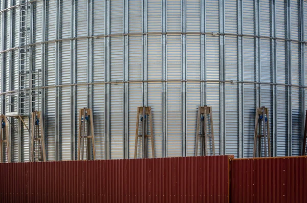 Industrial construction site. Construction of metal cylindrical silos for grain storage. Mechanical cargo winches lift the partially assembled grain silo.