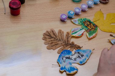 Sanatçı kurumuş yapraklarla resim çizer. Bir ayı yavrusu ve bir atın komik çizimleri. Akrilik boya ve guaj. Yetişkin bir kadın. İçeride. Seçici odak.