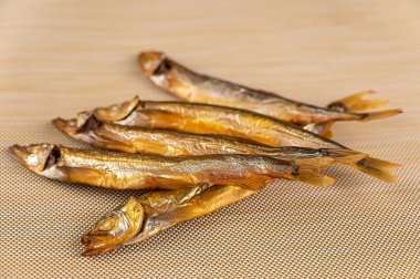 Bej bir arka planda tütsülenmiş kapelin. Yemeye hazır beş küçük balık. Deniz ürünleri..