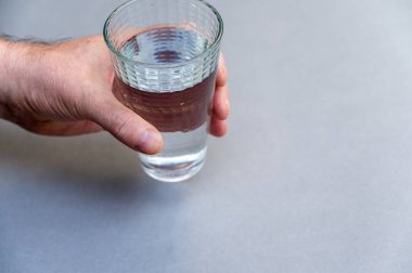 Bir adamın eli, arka planda gri bir zemine karşı uzun bir bardak su tutar. Koni şeklinde bir bardak berrak içme suyu. Seçici odaklanma. V