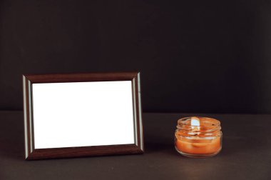 Yanan mumun yanındaki siyah hasara karşı koyu kahverengi boş bir fotoğraf çerçevesi. Cam bir kavanozda kırmızı ışık. Ahşap dikdörtgen fotoğraf çerçevesinin yatay konumu.