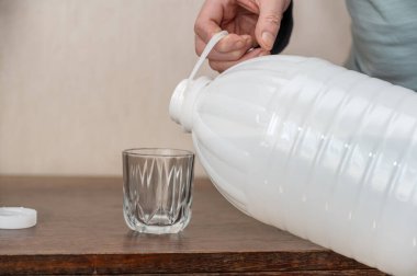 Bir adam bardağa su döker. Büyük, beyaz, plastik bir şişe taze su..