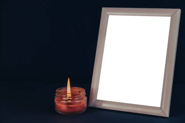 Yanan mumun yanındaki siyah hasarlı bölgenin önündeki boş fotoğraf çerçevesi. Cam bir kavanozda kırmızı mum yanıyor. Ahşap dikdörtgen fotoğraf çerçevesinin dikey konumu.
