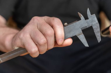Kalibreyi tutan bir adamın eli. Nesnelerin dış ve iç boyutlarını ve derinliklerini ölçmek için yüksek hassasiyetli metal bir aleti olan yetişkin bir adam.