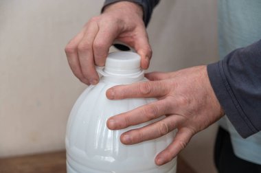 Bir adam beyaz bir şişe su açıyor. Adamın eli plastik şişenin mantarını tutuyor..