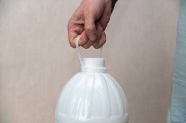 Bir adamın eli beyaz plastik bir şişenin sapını tutuyor. Büyük bir şişe içme suyu.