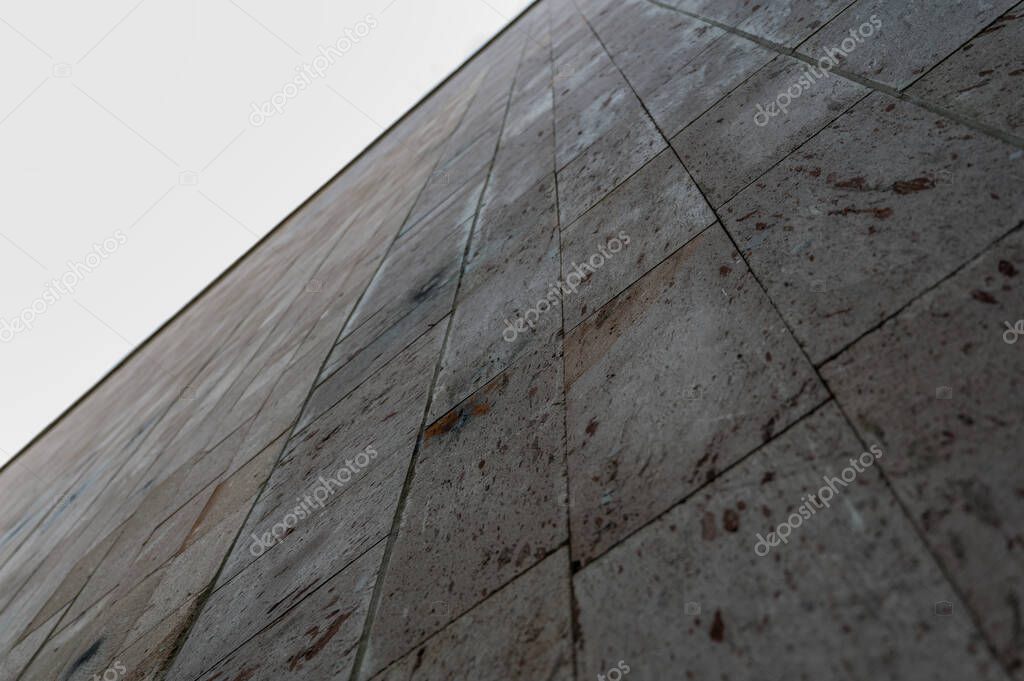 A view of the gray stone wall in the receding perspective. The outer wall of the building is covered with rectangular stone slabs. Daytime. Close-up. Selective focus.